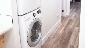 A laundry room with two stacked washing machines, a wooden floor, and a door leading to another room. - 7 Mins to Joshua Tree Park, Hot Tub · Sunset Jewel (Joshua Tree)