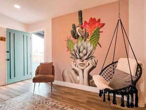A room with a hanging chair, a sofa, and a wall mural. - 7 Mins to Joshua Tree Park, Hot Tub · Sunset Jewel (Joshua Tree)