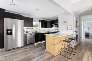A modern kitchen with dark cabinets, stainless steel appliances, a wooden island, and bar stools. - 7 Mins to Joshua Tree Park, Hot Tub · Sunset Jewel (Joshua Tree)