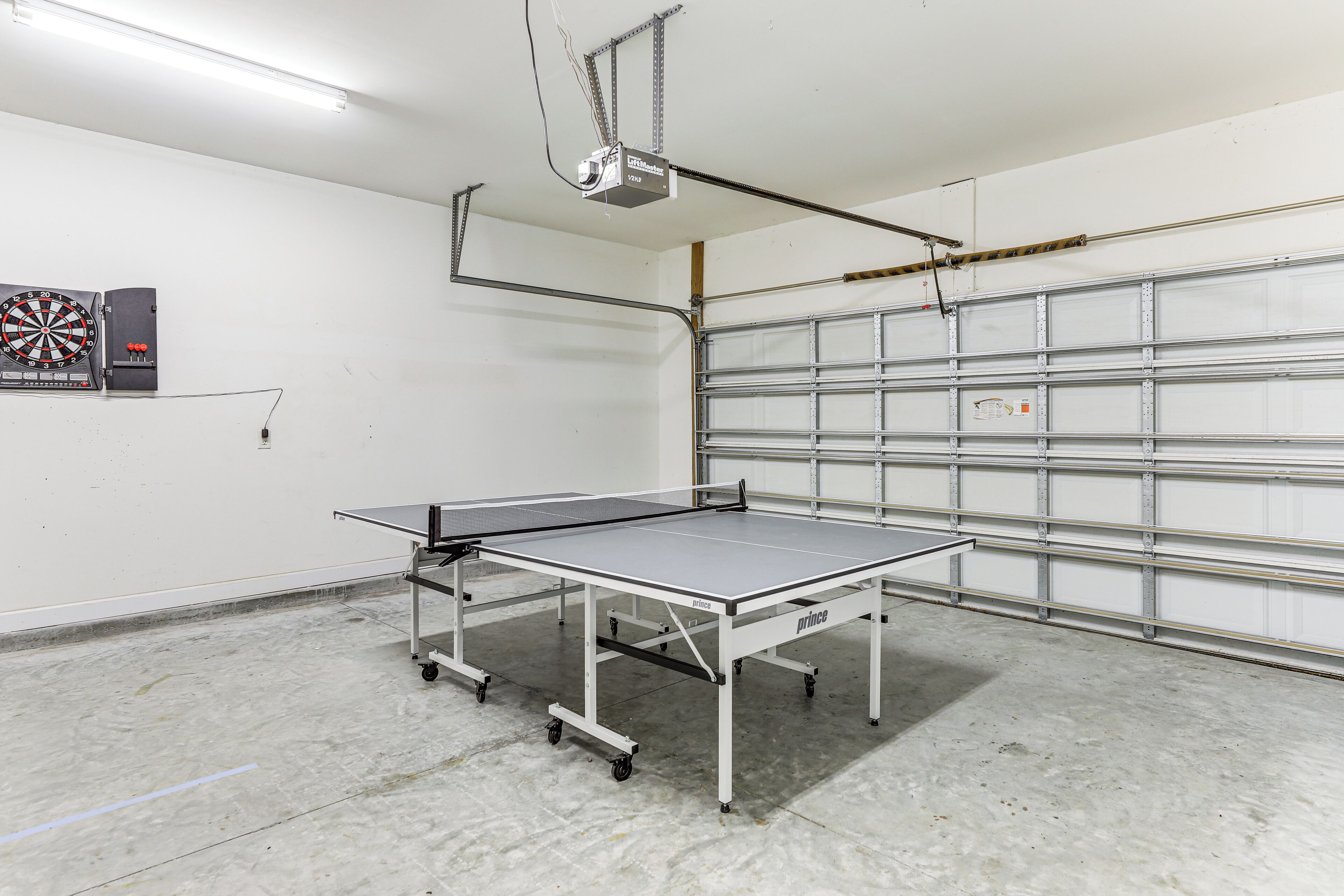 Una mesa de ping pong en un garaje con un dardo y un proyector montado en el techo.