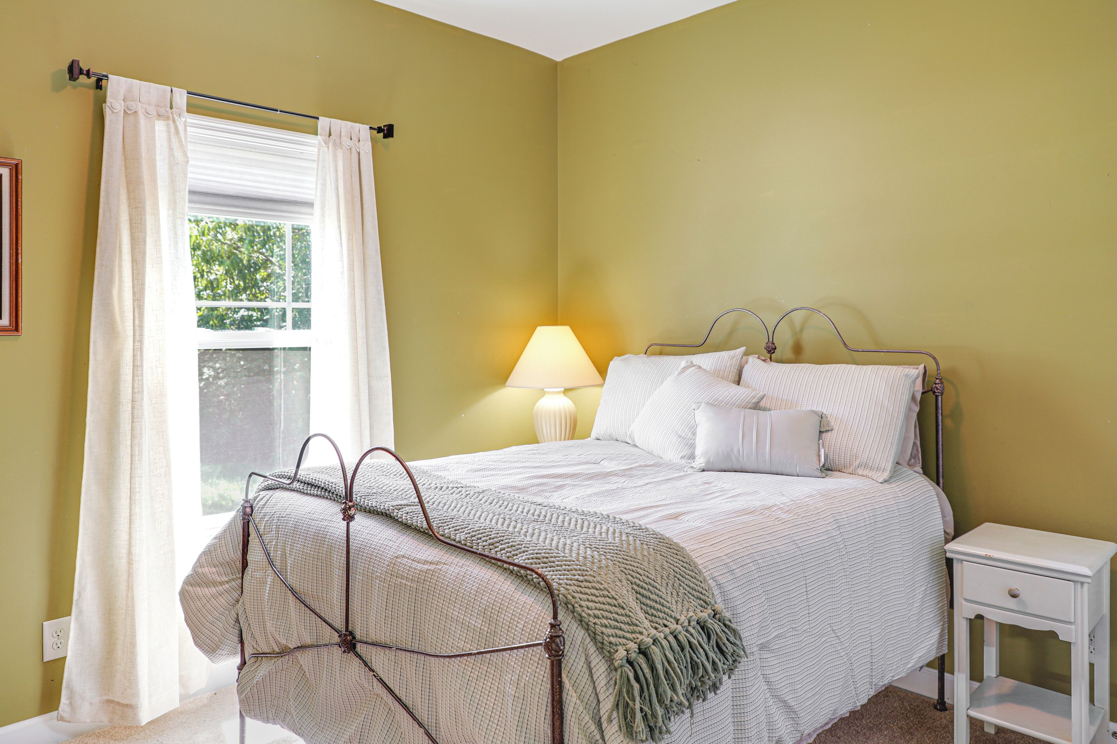 Une chambre à coucher avec un lit, une table de chevet, une lampe et une fenêtre avec des rideaux.