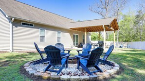 Ein Garten mit überdachter Terrasse, zwei Adirondack-Stühlen und einem Feuerkorb.