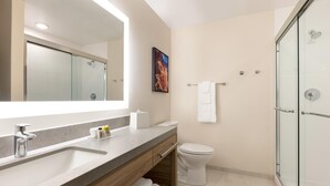 A modern bathroom with a large mirror, a sink, a toilet, and a glass-enclosed shower. - Candlewood Suites Oxford - Anniston By IHG (Oxford)
