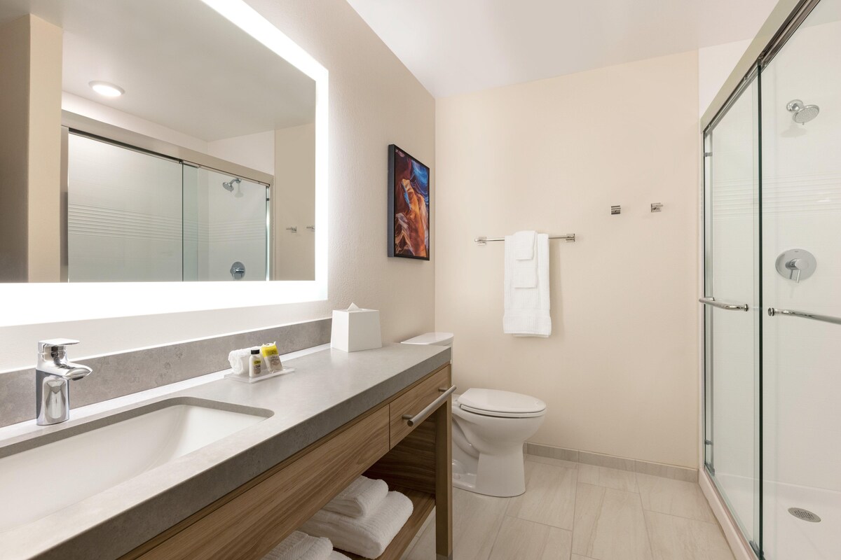 A modern bathroom with a large mirror, a sink, a toilet, and a glass-enclosed shower.