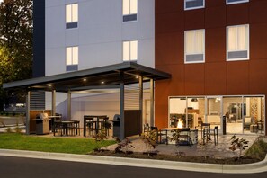 A modern building with a covered outdoor seating area, a barbecue grill, and a fire pit. - Candlewood Suites Oxford - Anniston By IHG (Oxford)