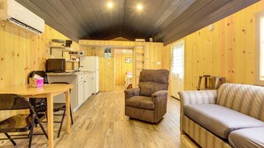 Un acogedor interior de cabaña con piso de madera, un sofá, una silla, una mesa de comedor y una kitchenette.