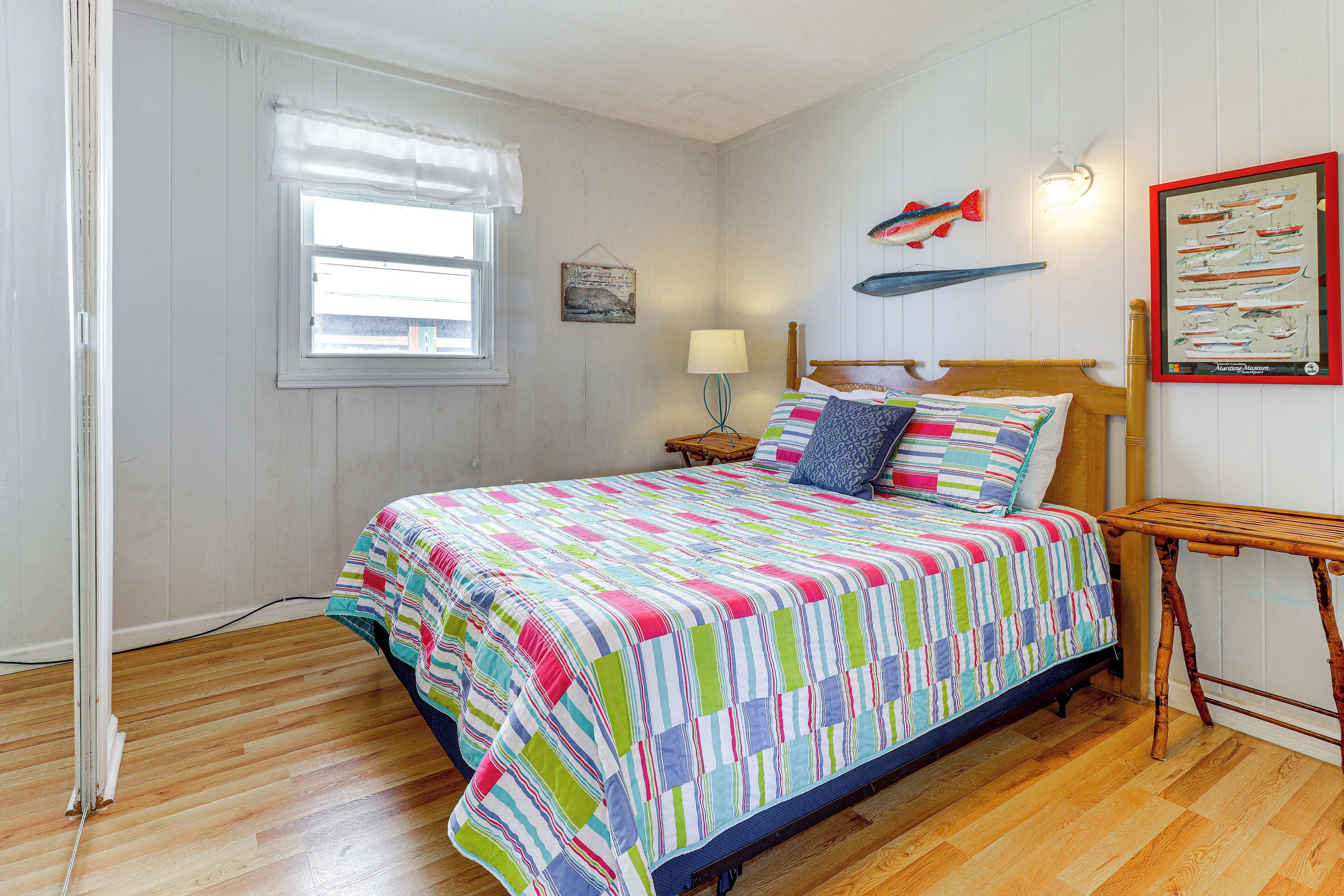 Un dormitorio con cama de madera, una ventana con persianas, una lámpara de pared y una ilustración enmarcada de un pez.