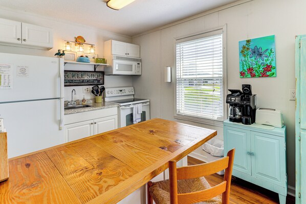 A kitchen with white cabinets, a wooden table, and a teal cabinet. - Oak Island Condo w/ Ocean View: Steps to Beach! (Oak Island)