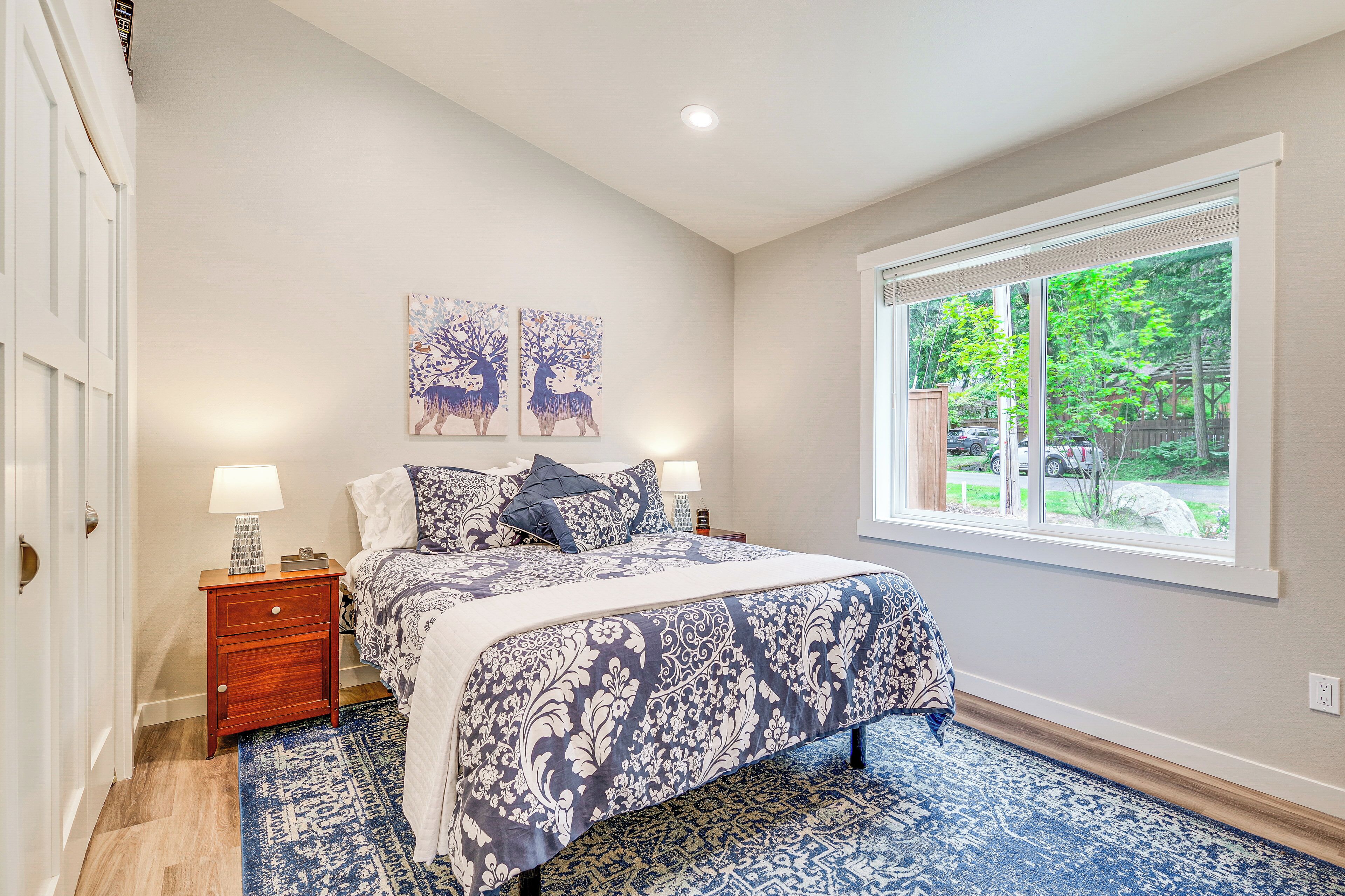 A bedroom with a large bed, a nightstand with a lamp, and two wall-mounted paintings of deer.