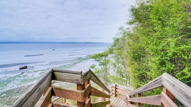 Eine Holztreppe führt zu einem Strand mit Blick auf das Meer und dichtes Grün.