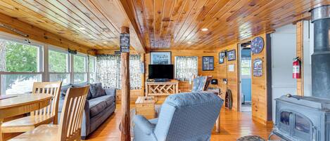 A cozy cabin interior with a wooden ceiling, a TV, a fireplace, and a dining area.