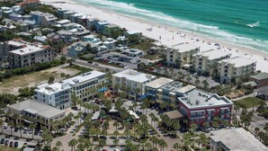 Luftaufnahme einer Küstenstadt mit Strandhotels, einem Parkplatz und einem Strand voller Menschen.