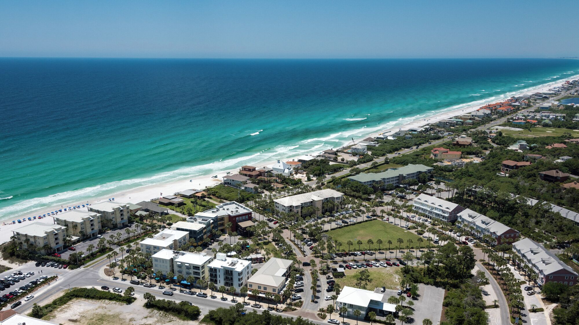 An aerial view of a coastal town with beachfront properties, a marina, and a mix of residential and commercial buildings.