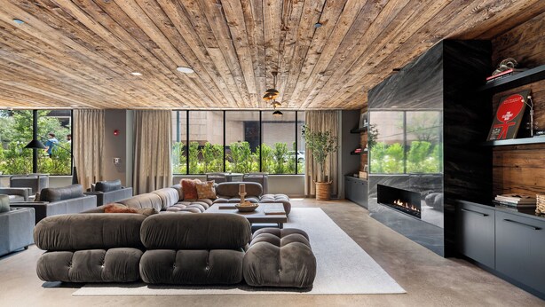 A modern living room with a large sectional sofa, a fireplace, and large windows offering a view of greenery. - Hyatus Luxury Residences Stamford (Stamford)