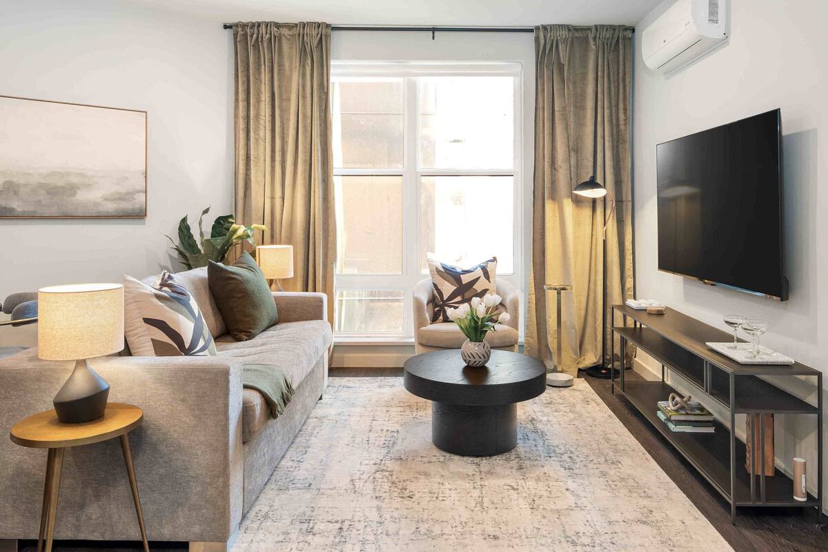 A modern living room with a sofa, a coffee table, a TV, and a large window with curtains.
