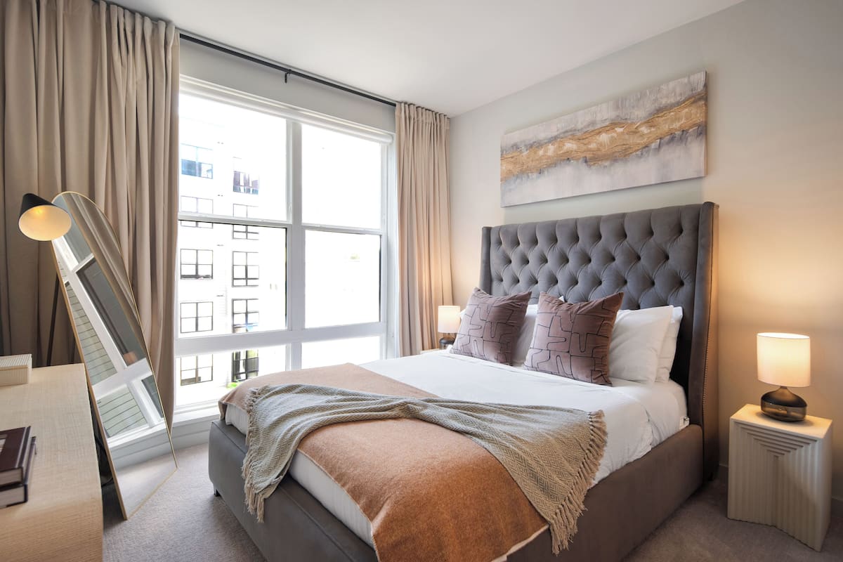 A neatly arranged bedroom with a large bed, a bedside table, a lamp, and a window with curtains.