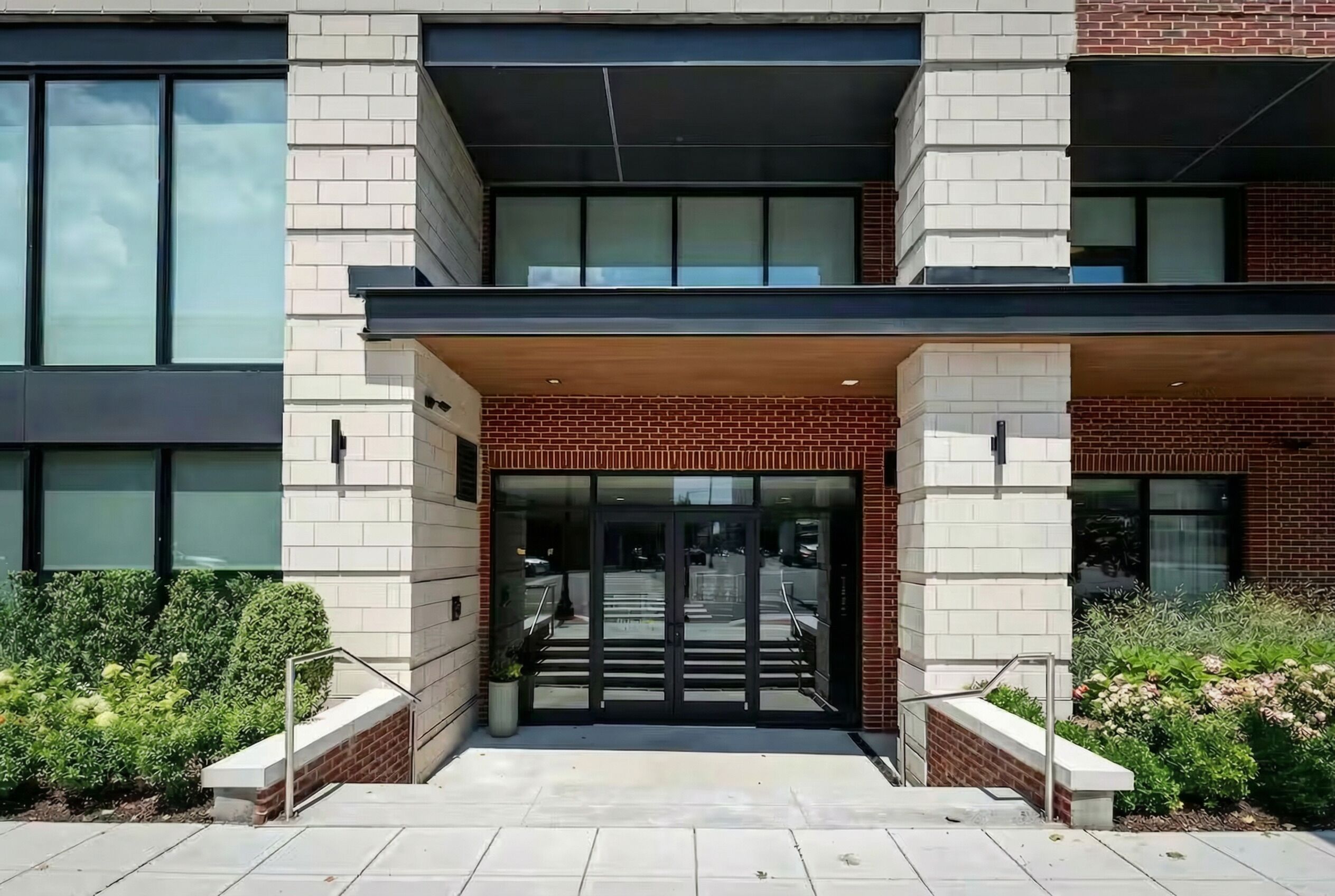 A modern building entrance with a glass door, brick facade, and a small covered area above the door.