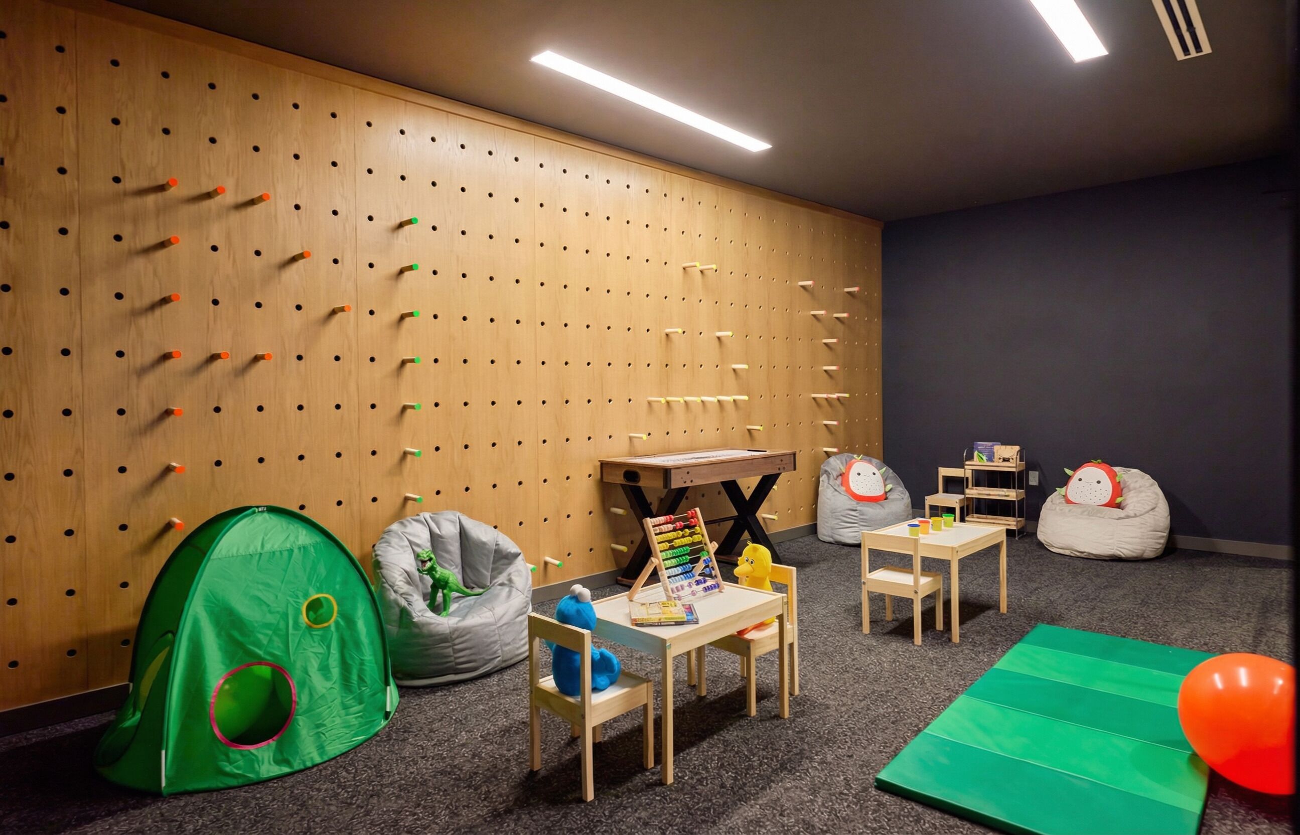 A playroom with a pegboard wall, a green tent, bean bags, a small table with toys, and a green mat on the floor.