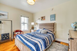 Ein Schlafzimmer mit einem Bett, einem Schreibtisch, einem Stuhl, einem Ventilator und einem Globus auf einer Kommode.