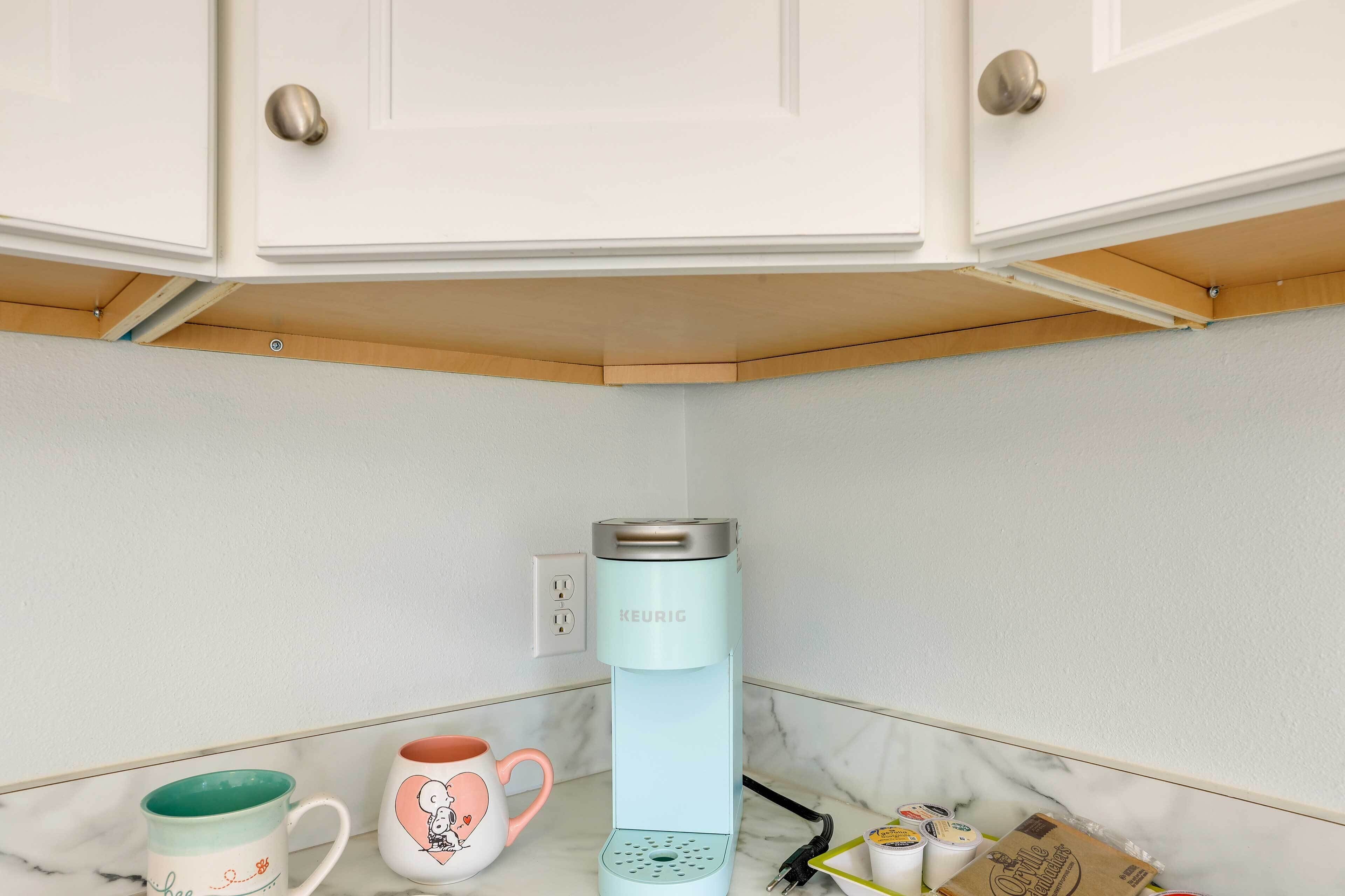 Une cuisine avec des meubles blancs, un plan de travail en marbre, une machine à café Keurig et deux tasses.