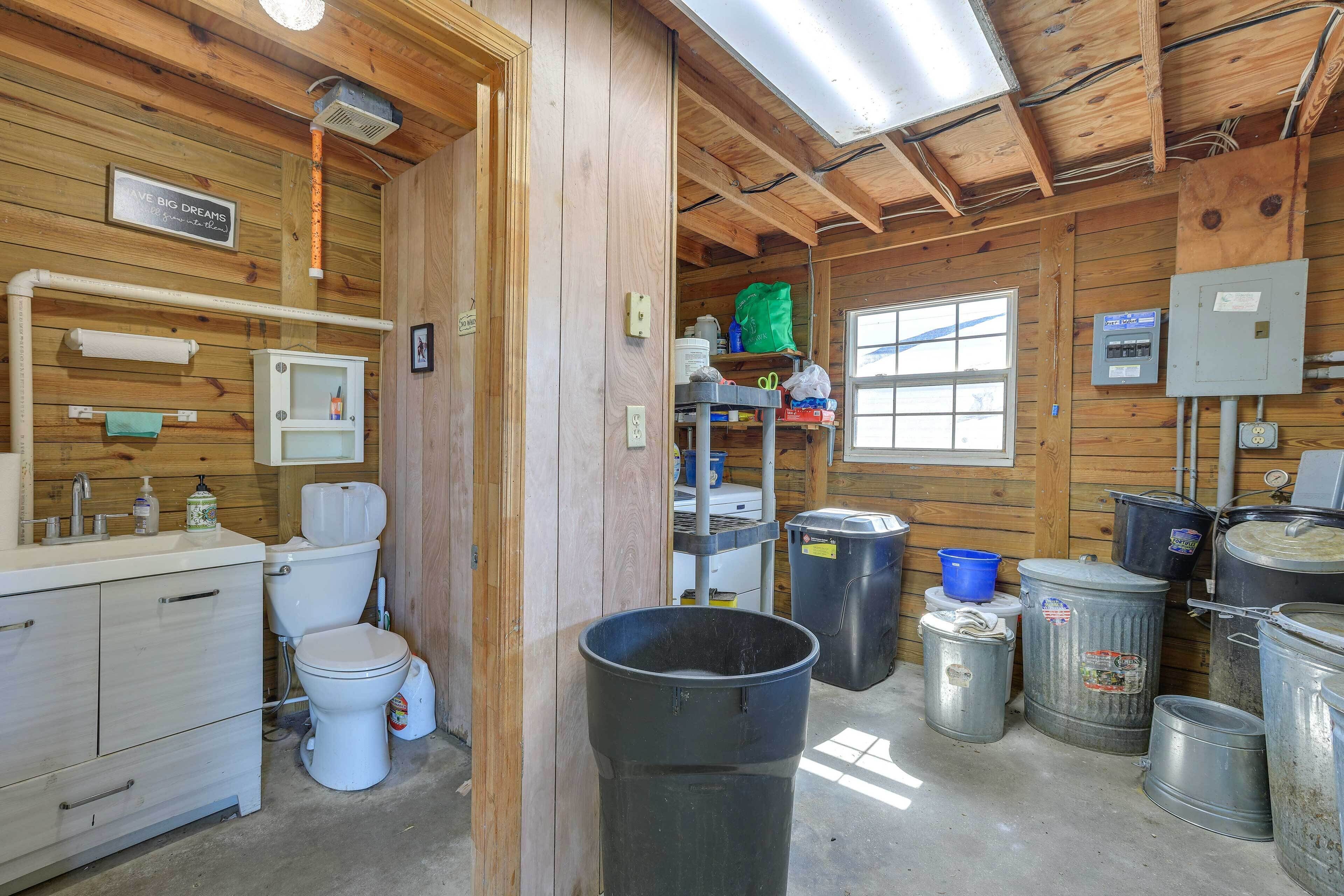 Interior rústico de una cabaña con paredes de madera, un inodoro blanco, un lavabo y varios contenedores de almacenamiento.