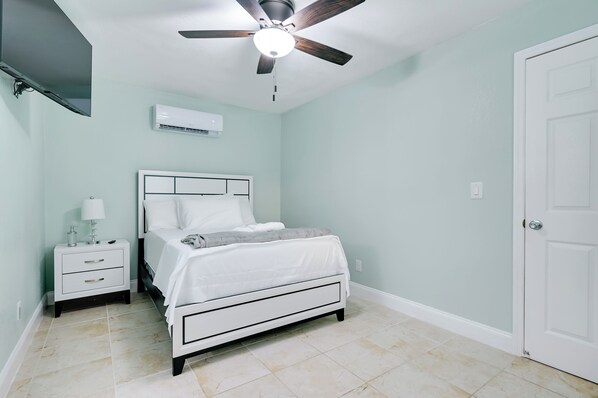Un dormitorio con cama, mesita de noche, lámpara, ventilador de techo y aire acondicionado.