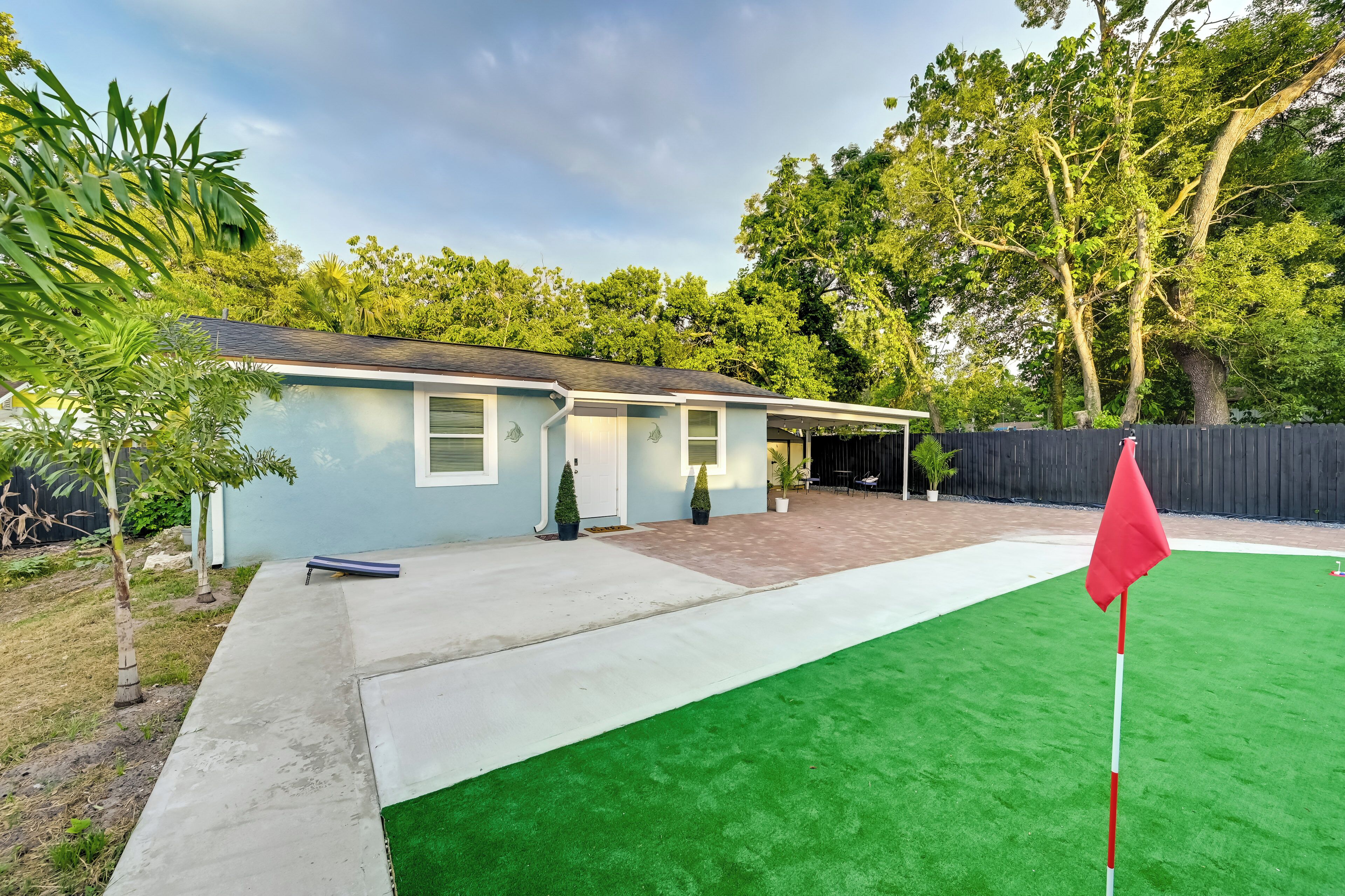 A residential property with a covered patio, artificial green turf, and a red flag marking a golf hole.