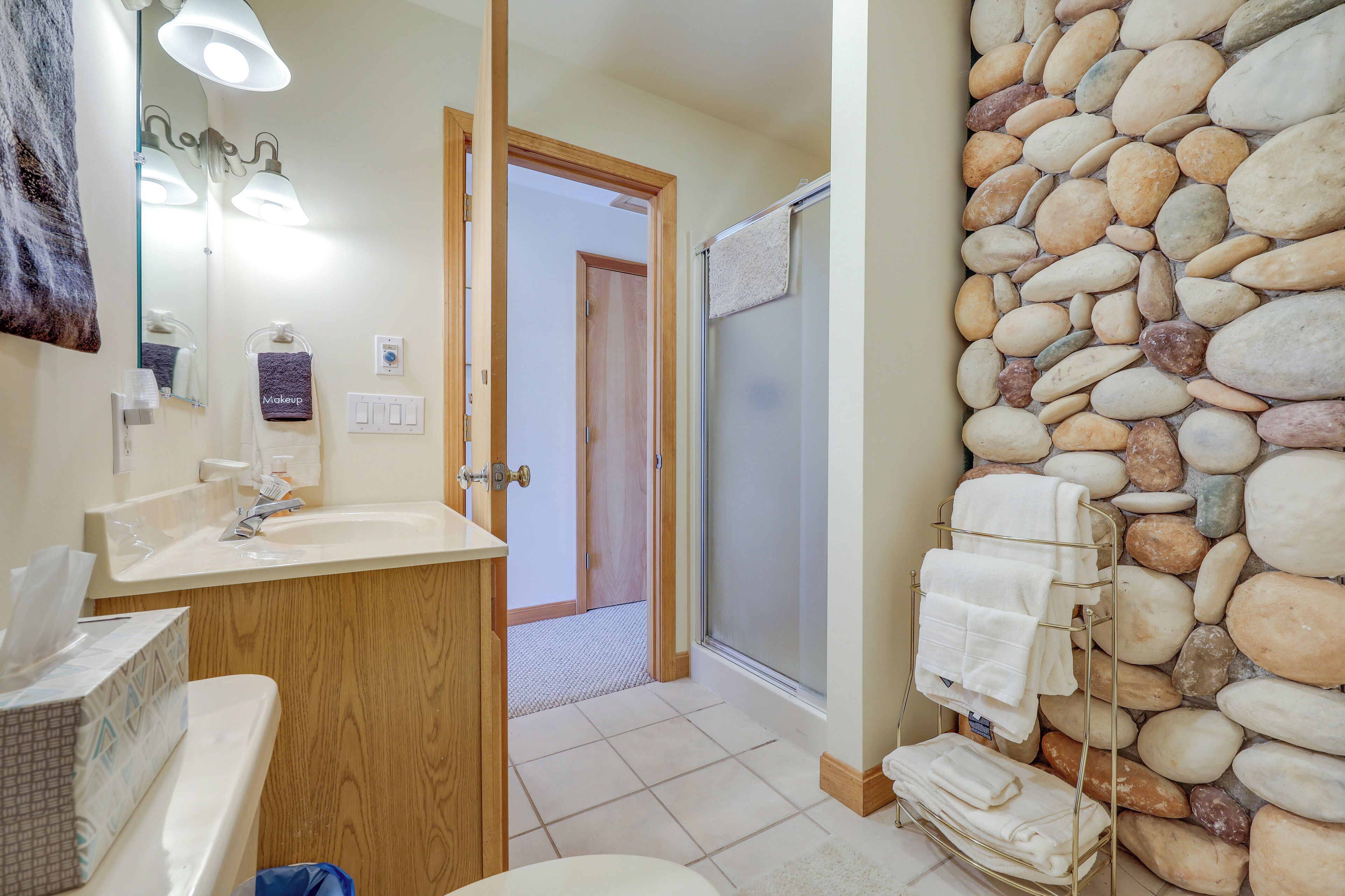 A bathroom with a wooden vanity, a sink, a mirror, and a towel rack against a stone wall.