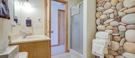 A bathroom with a wooden vanity, a sink, a mirror, and a towel rack against a stone wall.