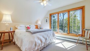 A bedroom with a large window, a ceiling fan, a bedside table with a lamp, and a chair. - Serene Steuben Home w/ Scenic Ocean Views! (Steuben)