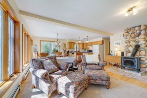 A spacious living room with a fireplace, a dining area, and a kitchen with wooden cabinets. - Serene Steuben Home w/ Scenic Ocean Views! (Steuben)