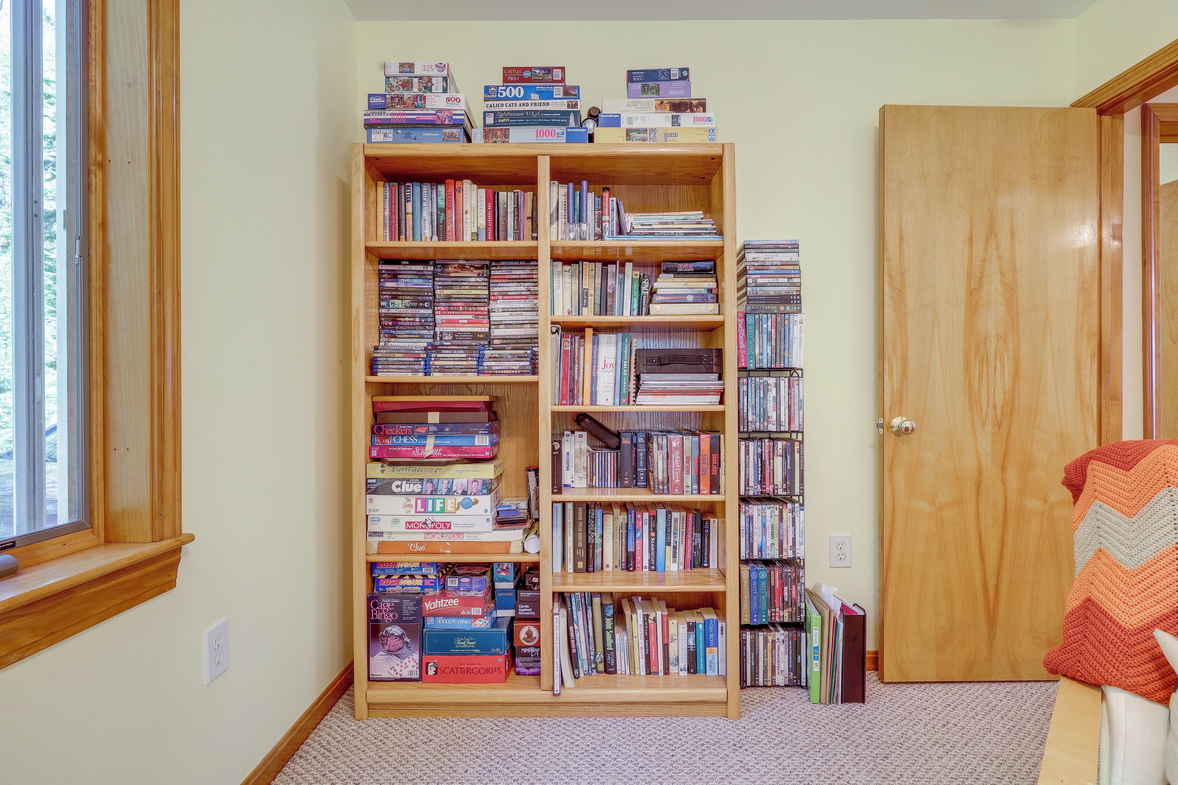 Une pièce dotée d’une grande bibliothèque remplie de livres et de jeux de société, d’une fenêtre et d’une porte.