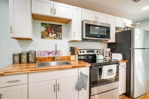 A modern kitchen with white cabinets, a stainless steel refrigerator, a microwave, and a stove. There are three metal containers on the counter, and a sign that says "RISE & SHINE". - Front Royal Studio w/ Mtn Views & Brick Oven (Front Royal)