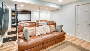 A living room with a brown leather sofa, a treadmill, and a bookshelf with children's toys. - Front Royal Studio w/ Mtn Views & Brick Oven (Front Royal)