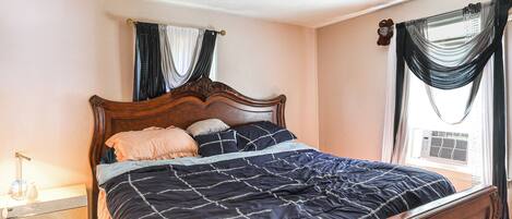 A bedroom with a wooden bed, a nightstand, a window with curtains, and an air conditioning unit.