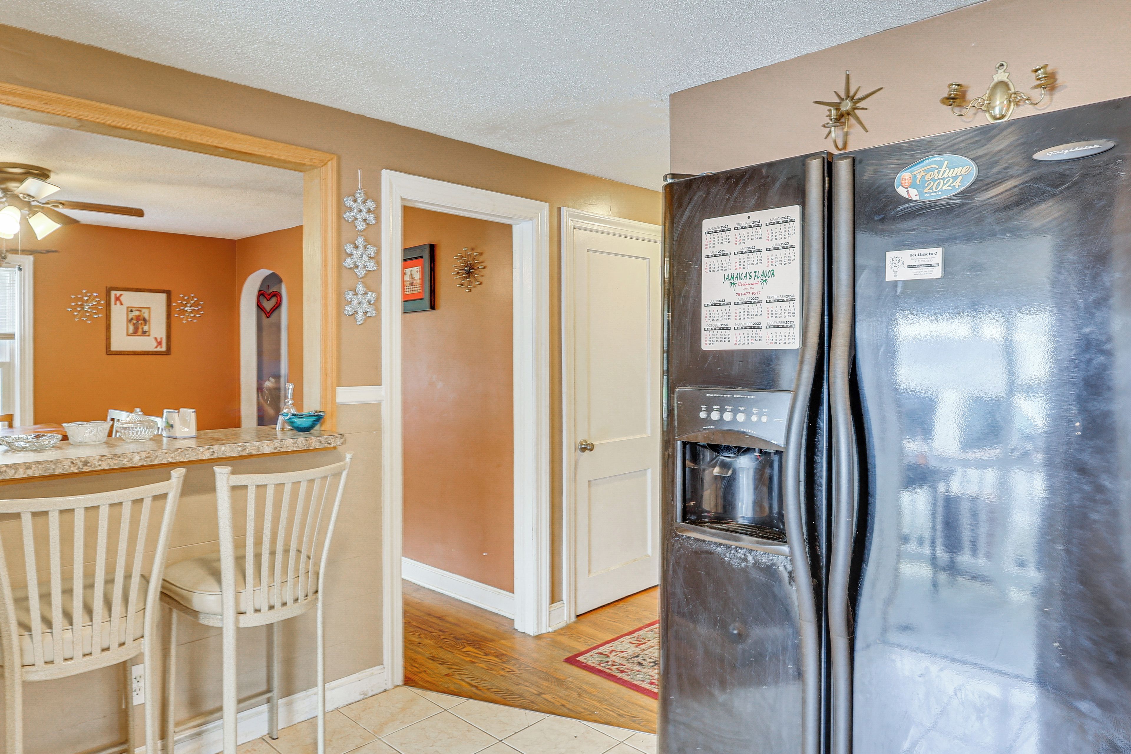 A kitchen with a refrigerator, a sink, and a dining area with chairs.