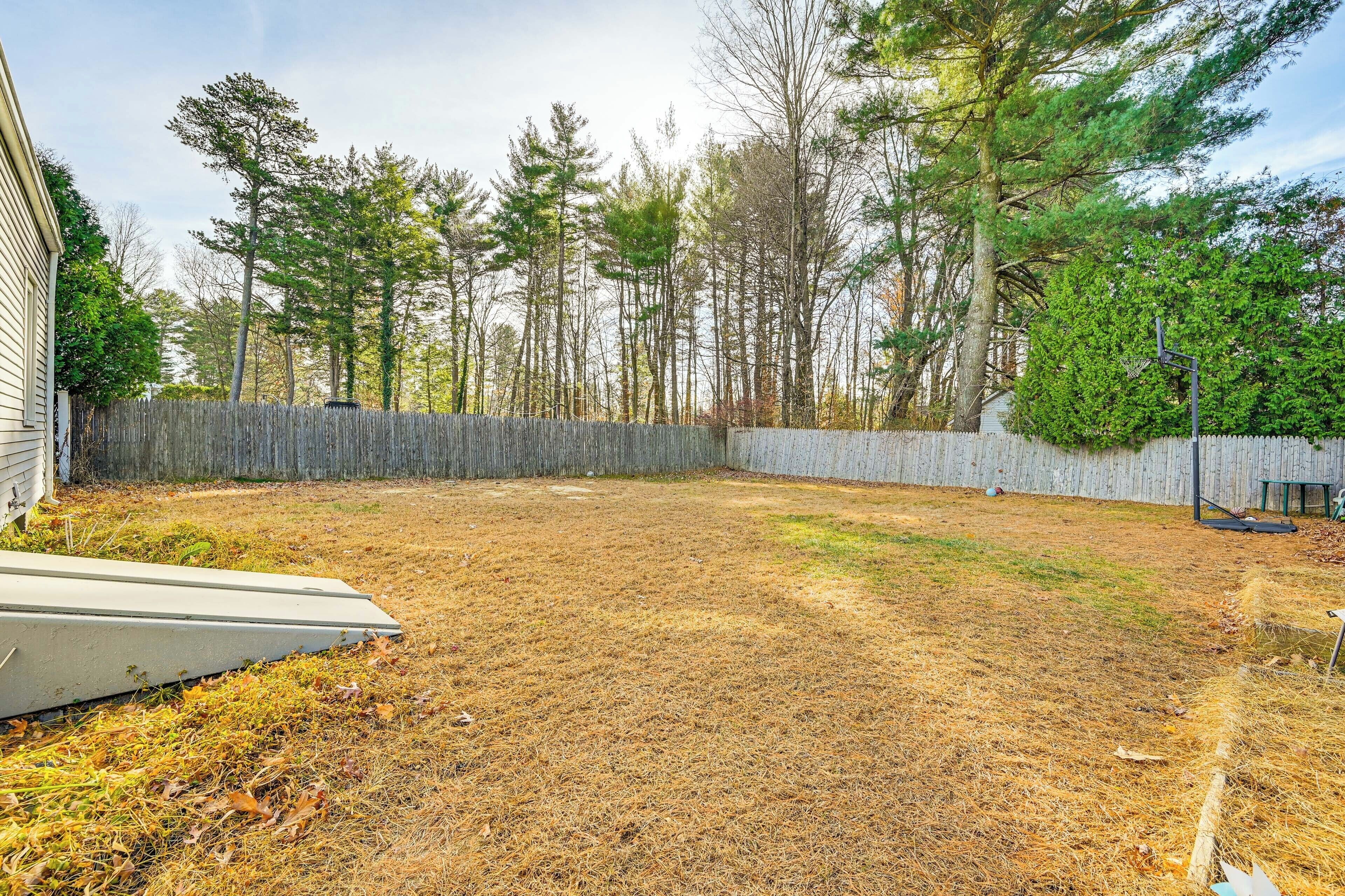 A backyard with a wooden fence, a trampoline, and a house in the background.