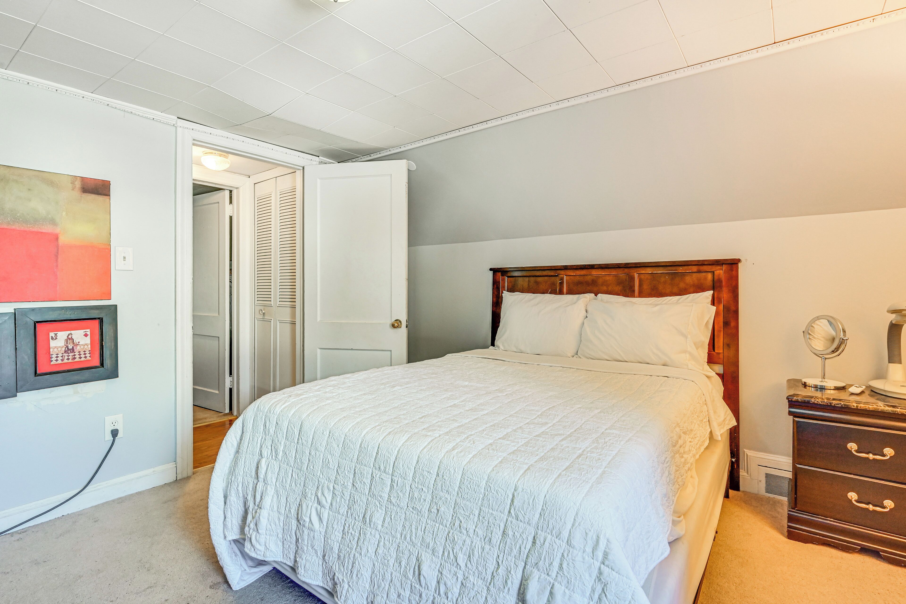 Ein Schlafzimmer mit einem Bett, einem Schminktisch, einem Spiegel und einer Tür zu einem anderen Raum.