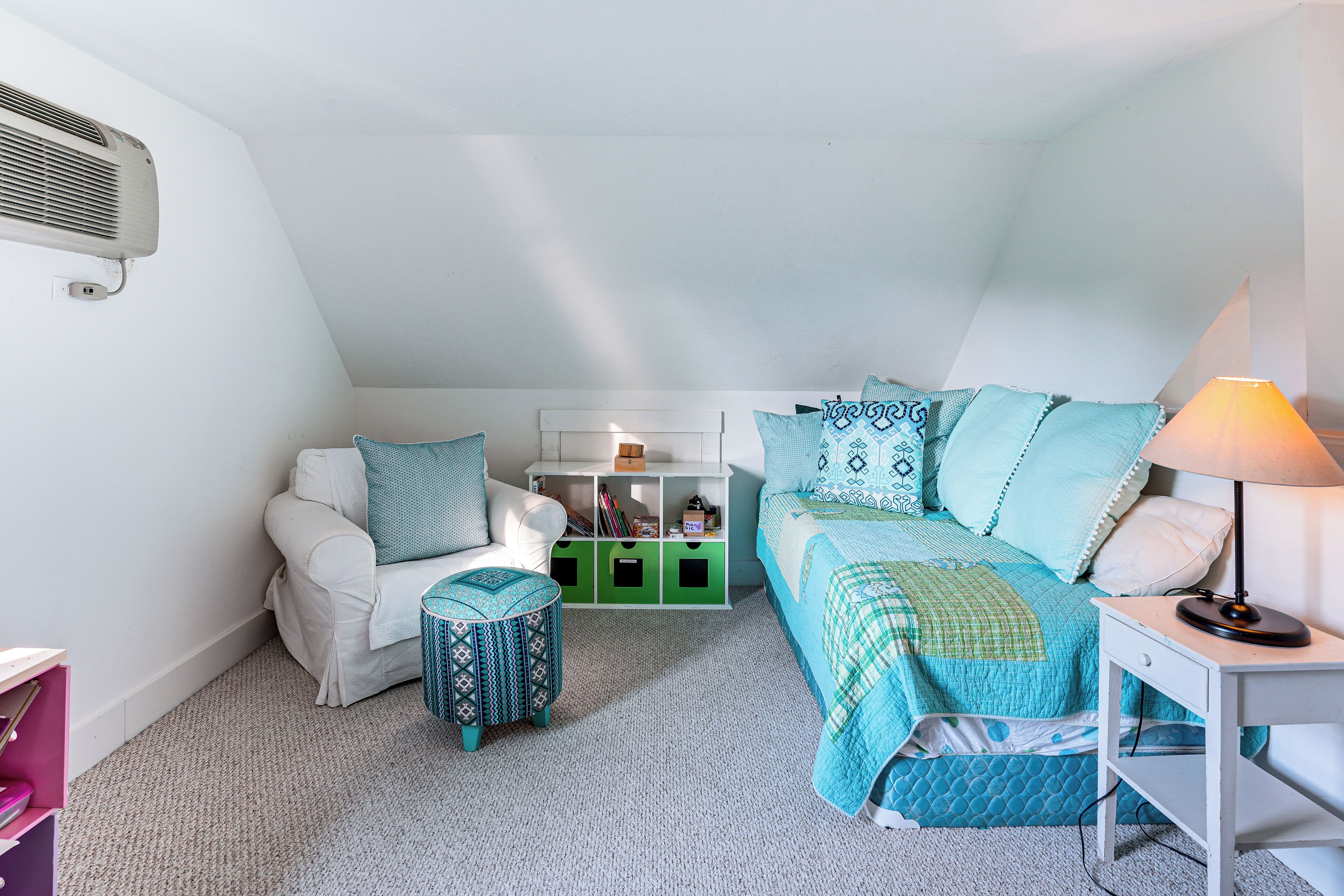 A bedroom with a white ceiling, a white sofa, a green storage unit, a bed with blue bedding, and a bedside table with a lamp.