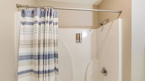 A shower with a striped curtain, a handheld showerhead, and a wall-mounted faucet.