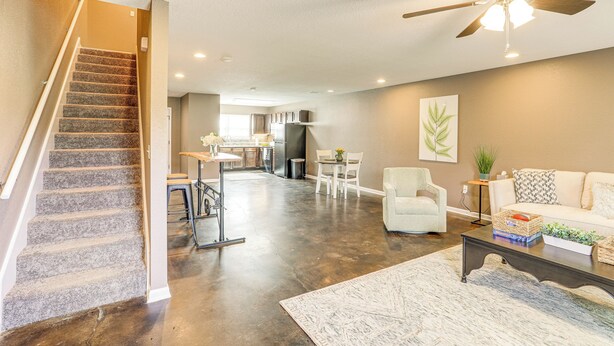 A spacious living area with a staircase, a ceiling fan, a kitchen in the background, and a dining area.