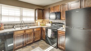 A kitchen with wooden cabinets, a stainless steel sink, a black refrigerator, and a stove.