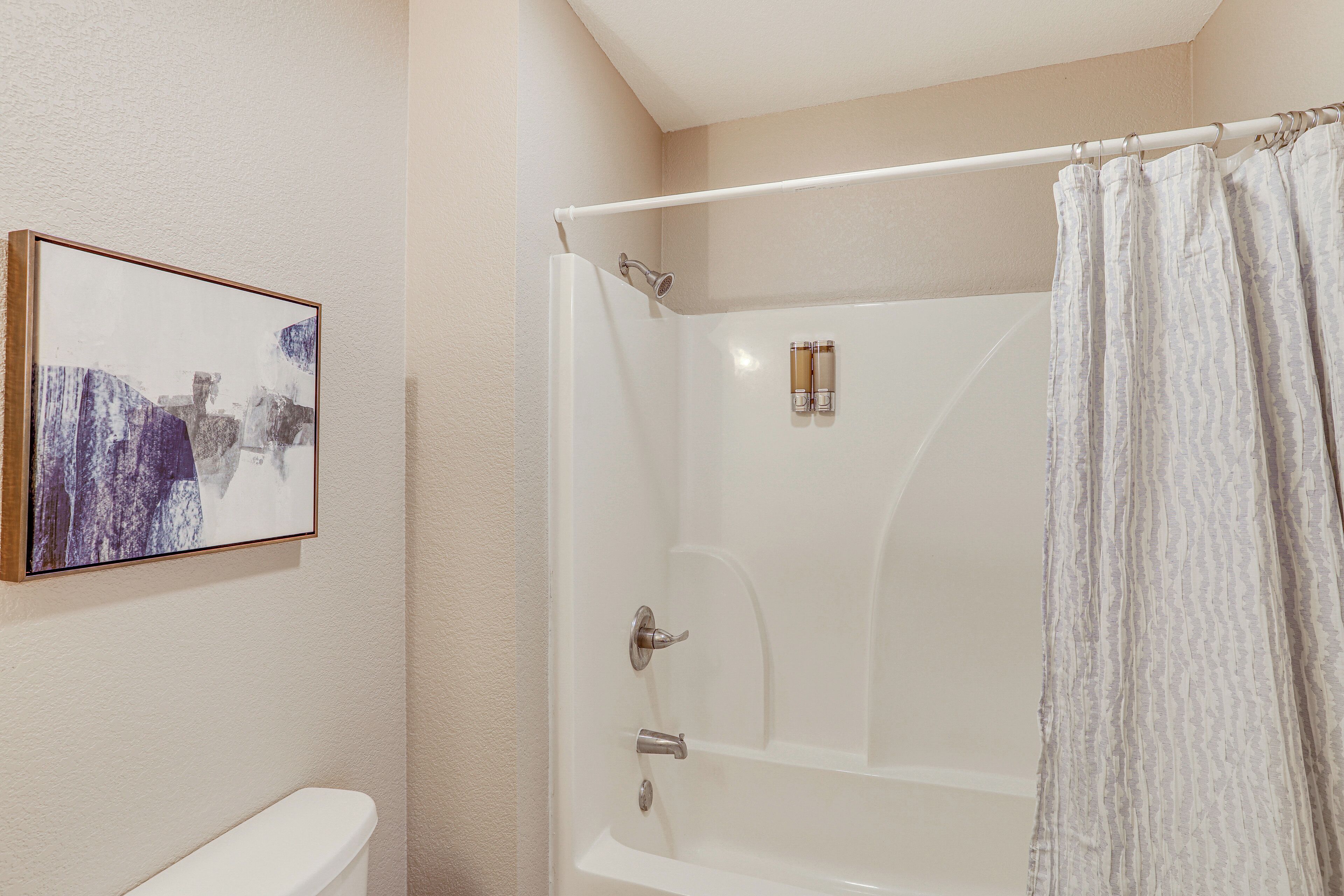 A bathroom with a bathtub, shower, and toilet. There is a framed artwork on the wall.