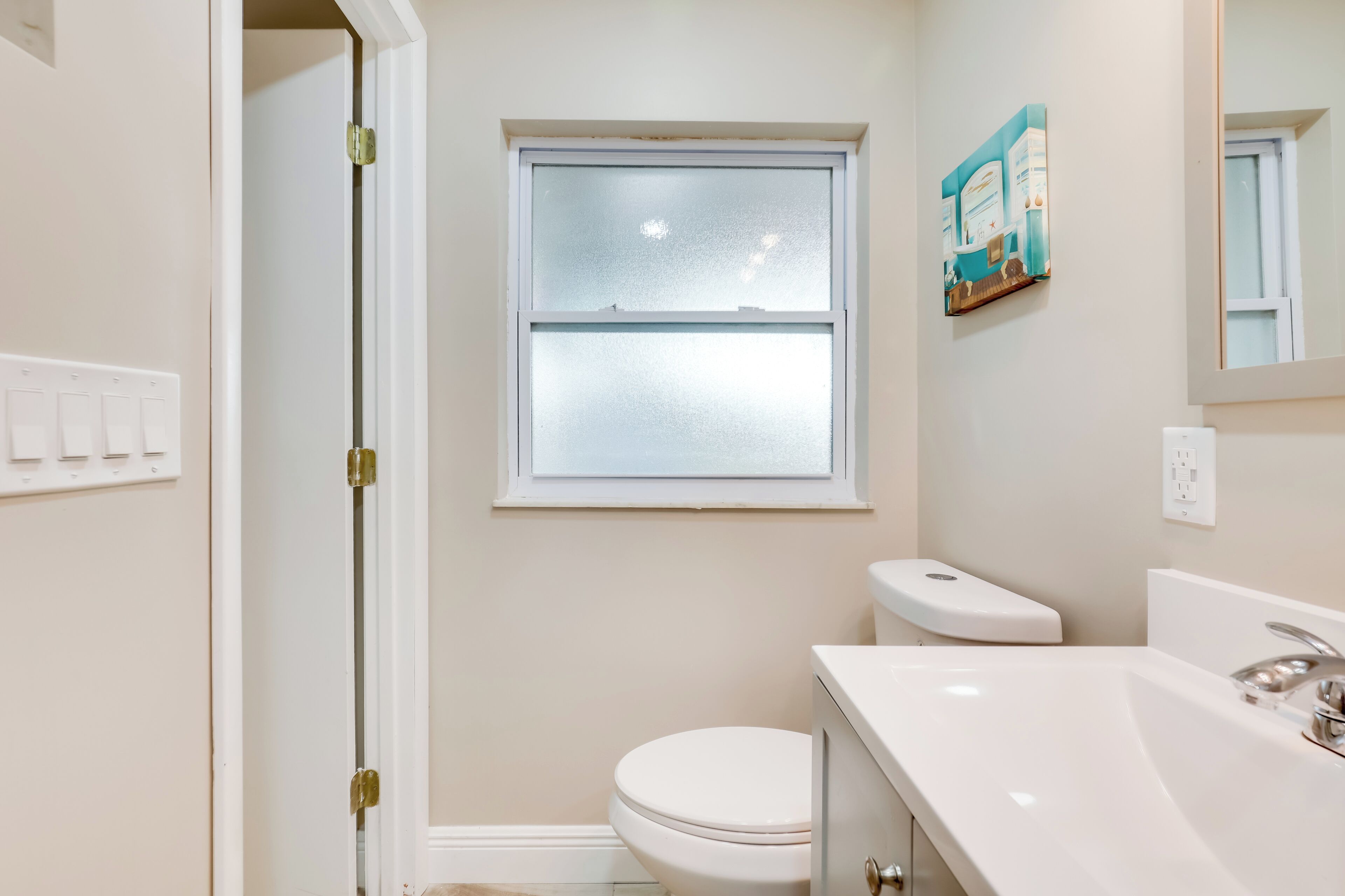 A bathroom with a toilet, a sink, a window, and a door.