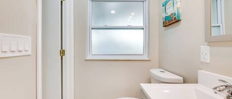 A bathroom with a toilet, a sink, a window, and a door.