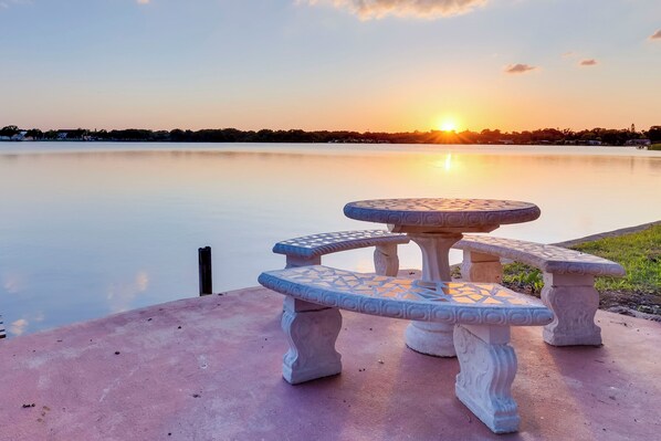 Un banco de piedra con diseños intrincados, ubicado junto a un lago tranquilo al atardecer.