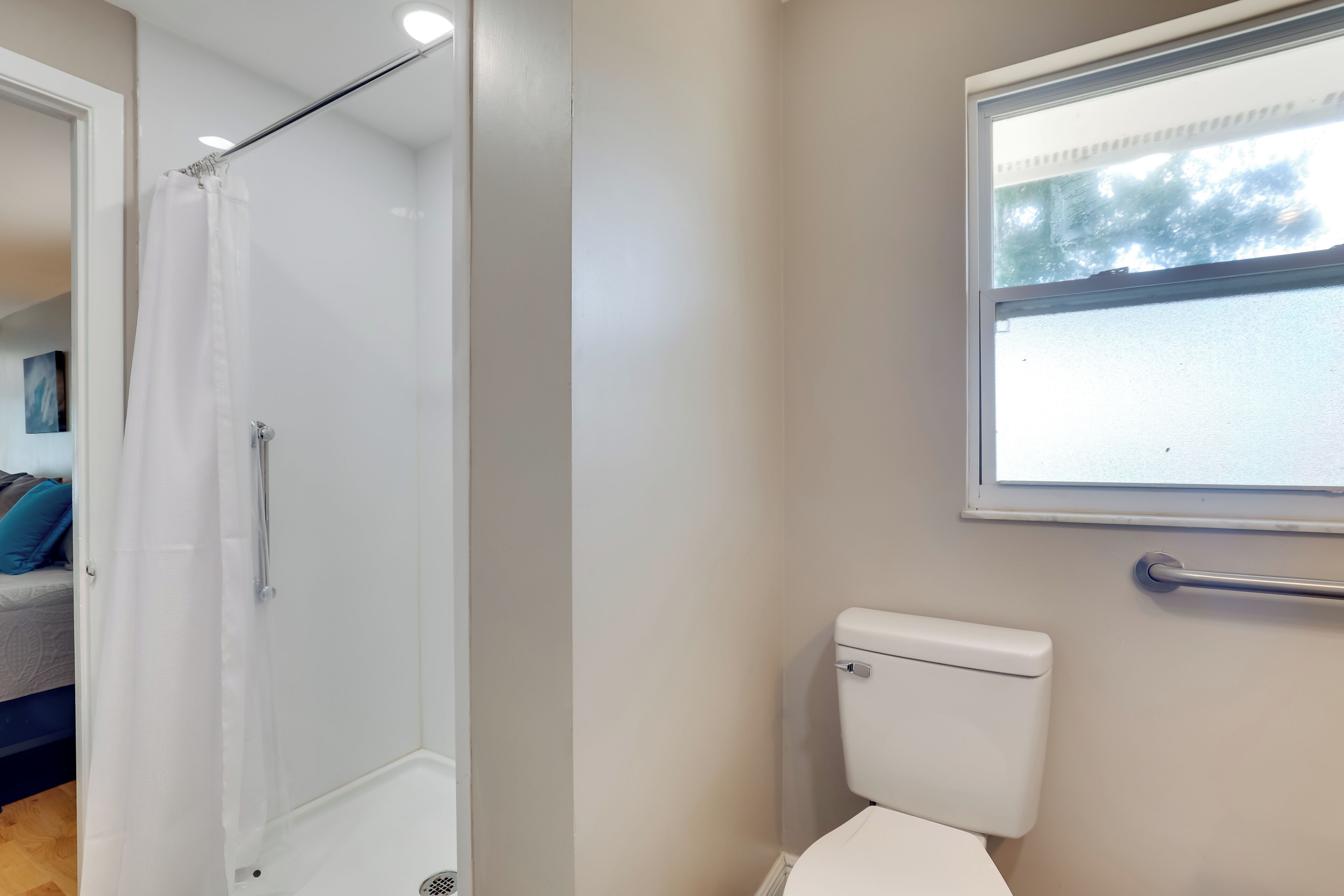 A bathroom with a shower, toilet, and window.