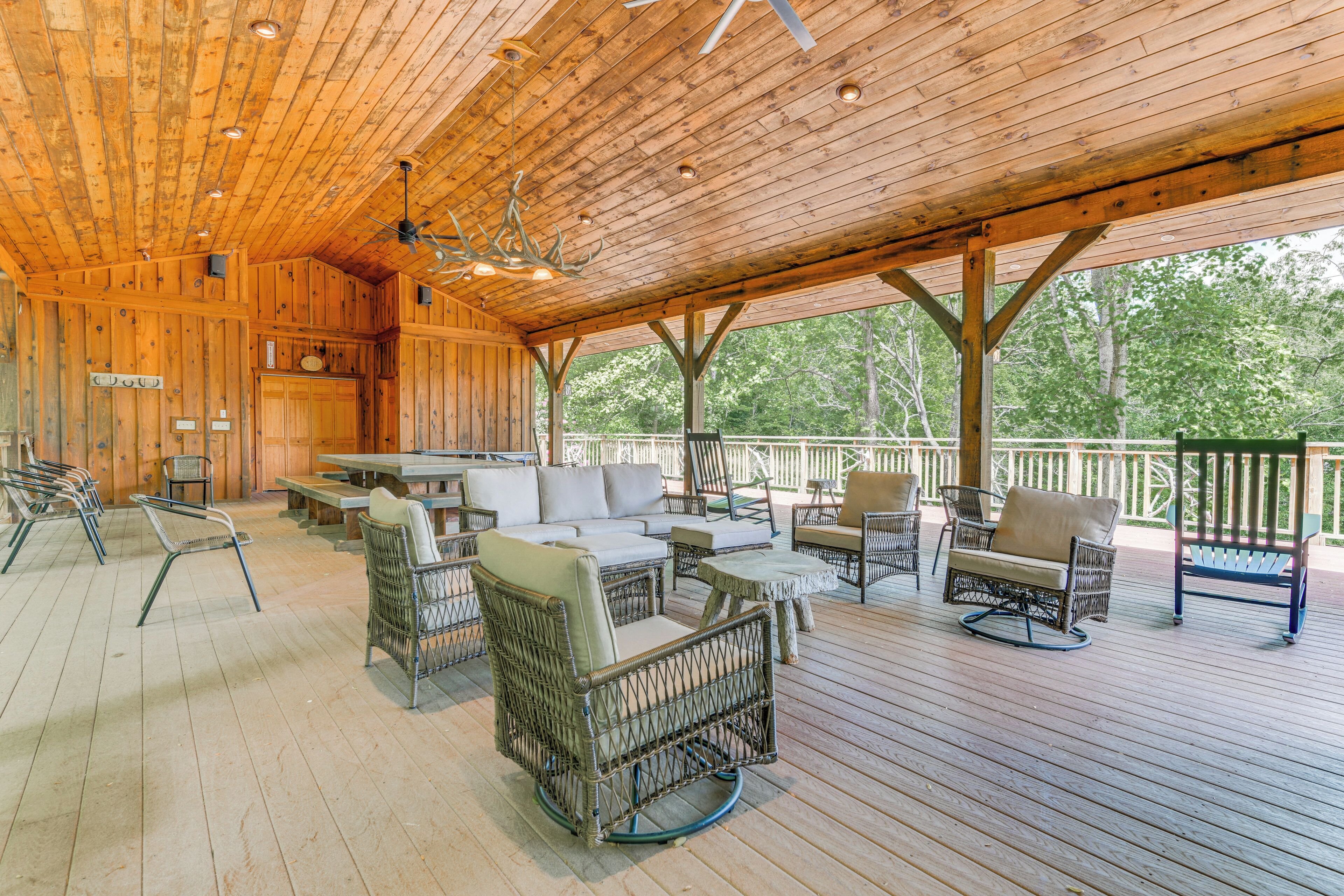 A covered outdoor area with wicker furniture, a wooden ceiling, and a view of trees.