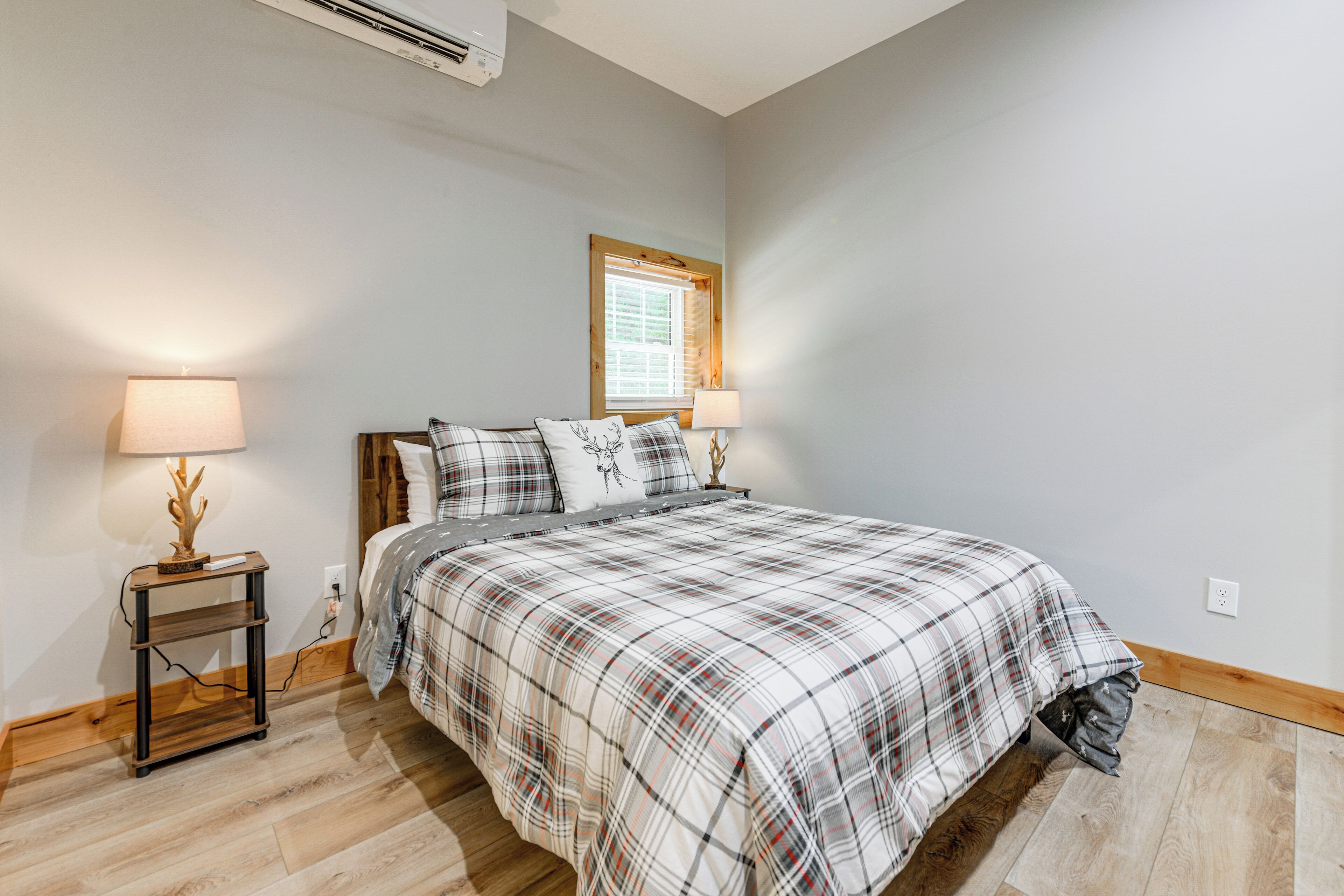 A bedroom with a bed, two bedside lamps, a window, and a wooden floor.