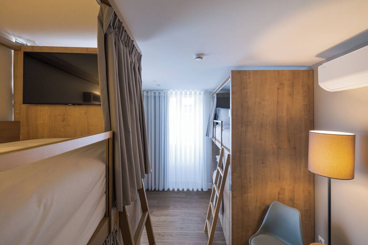 A narrow hotel corridor with bunk beds on one side and a desk area with a lamp on the other.